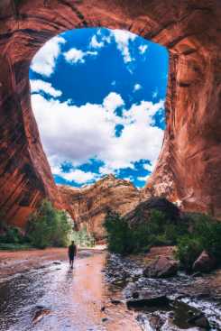 Person walking down a shallow river under a rock tunnel